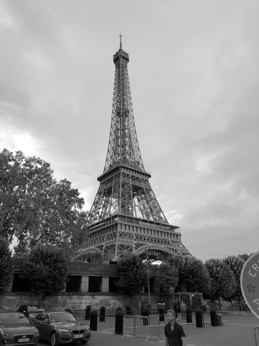 Students stand before the Eiffel Tower and gaze up at the architecture.