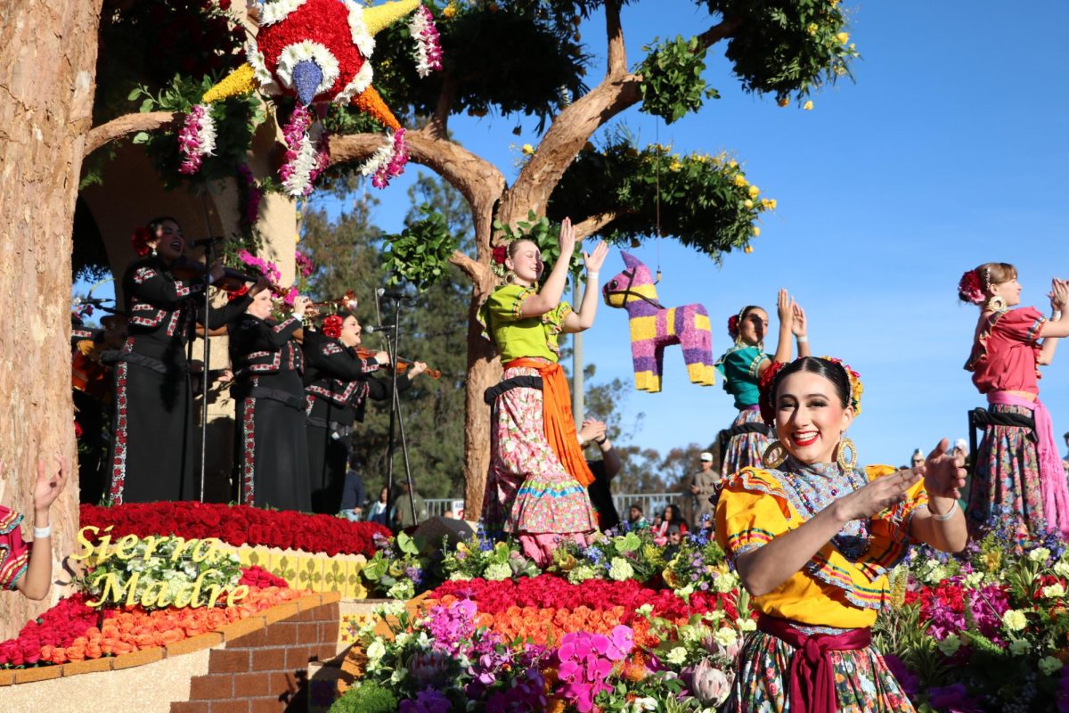 A mariachi band plays on The Sierra Madre Rose Float while dancers walk the street. The dancers walk up to spectators and bring an energy that matches the flowers on the float.