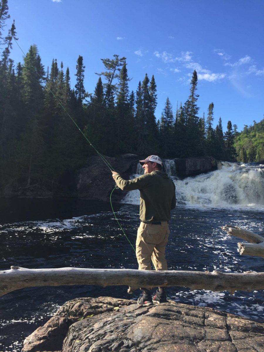 Teacher and Fly Fishing Club adviser Mr. Nick Plazak is seen fishing near a body of water.