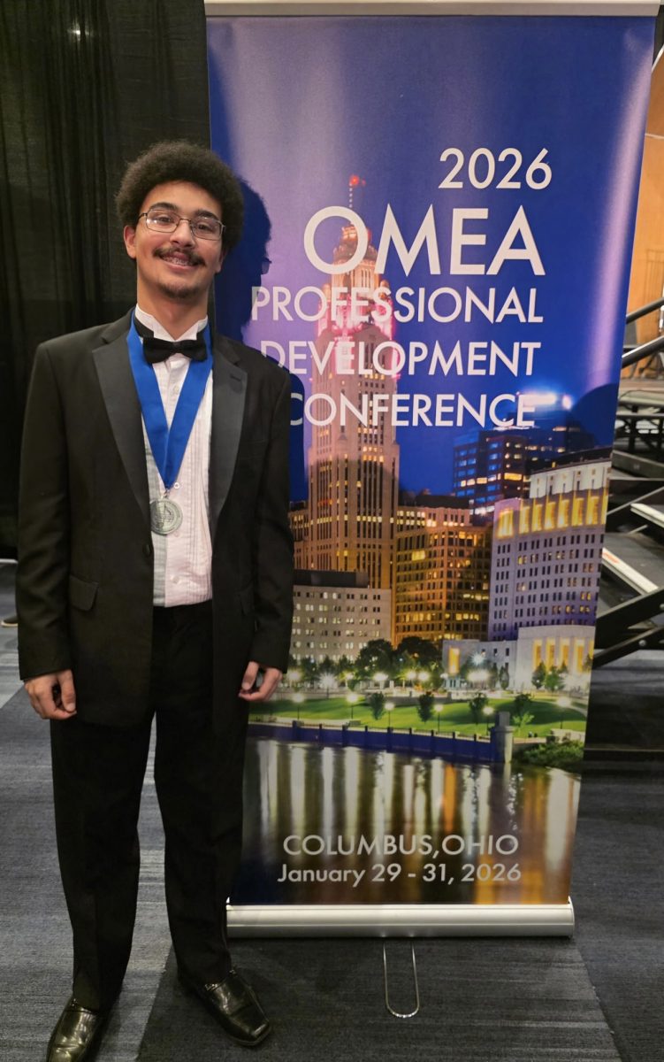 Senior Micah Hayes poses in front of a banner at OMEA’s annual music and education conference. 